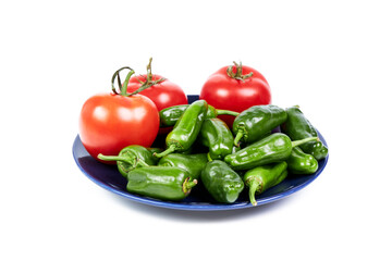 Red tomatoes next to green peppers on a blue plate on a white background. Healthy food concept