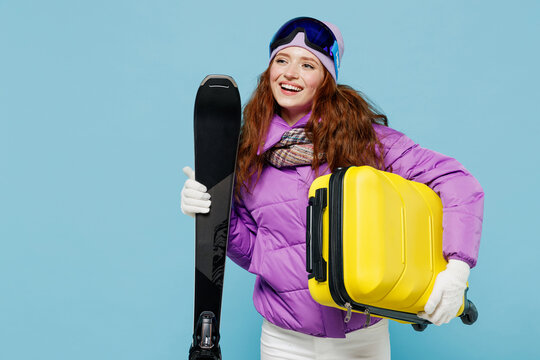 Traveler pensive tourist woman in ski windbreaker jacket goggles hold valise suitacase isolated on plain blue background studio Passenger travel abroad on weekends getaway Air flight journey concept.