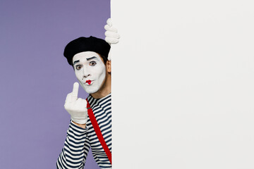 Crazy young mime man with white face mask wears striped shirt beret looking from behind white wall...