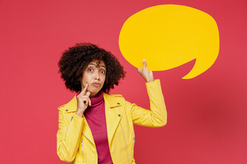 Pensive minded young curly black latin woman 20s years old wear yellow jacket hold in hand empty blank Say cloud speech bubble for promotional content isolated on plain red background studio portrait