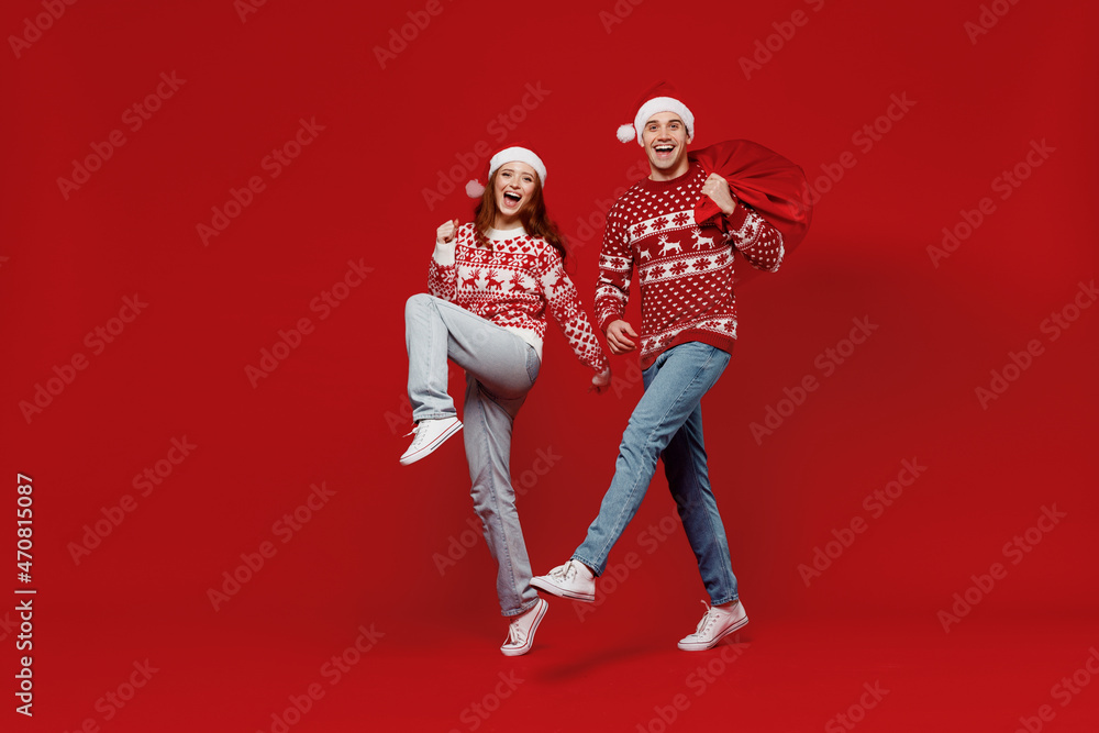 Poster Full body smiling young couple friends two man woman 20s in sweater hat hold gift bag do winner gesture isolated on plain red background Happy New Year 2022 celebration merry ho x-mas holiday concept.