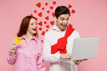 Young fun couple two friends woman man wear shirt using laptop pc computer hold credit bank card do online shopping isolated on plain pink background. Valentine's Day birthday holiday party concept.