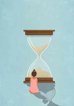 Girl looking at sand falling in large hourglass
