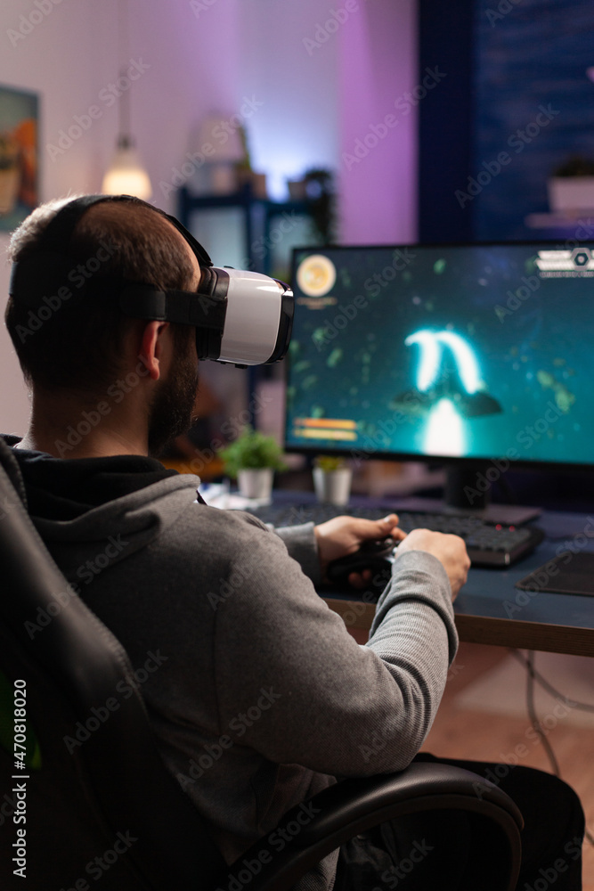 Wall mural Gamer using vr glasses and controller to play video games. Man with virtual reality goggles holding joystick in front of computer, playing online game. Player having fun with games.