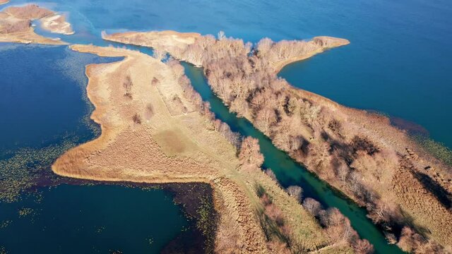 River mouth - landform caused by sediment deposition where stream Ljuca flows into lake Plav water in Montenegro. Peninsula or promontory split into two halves. Aerial drone view on a sunny day.