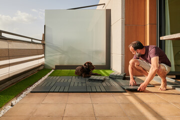 middle-aged bearded man looking at his Labrador retriever dog while assembling his new floor on the terrace of his house