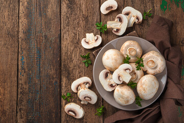 Raw mushrooms in a plate on a wooden background. Top view, copy space.