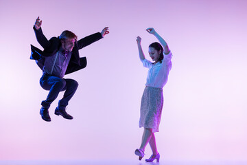 Fototapeta na wymiar Couple of dancers, young man and woman in vintage retro style outfits dancing swing dance isolated on lilac color background in neon light