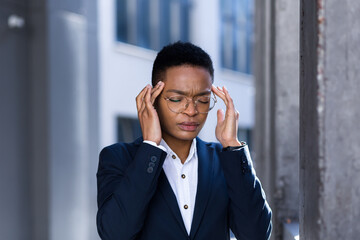 Young business woman has a severe headache, African American woman came out of the office, holding hands behind her head, migraine