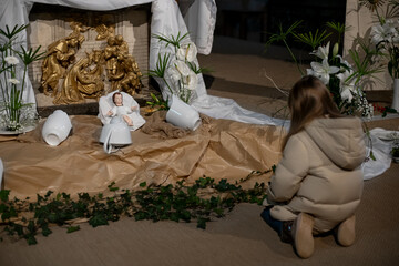 A girl looks at christmas creche with Joseph Mary and small Jesus in a crib