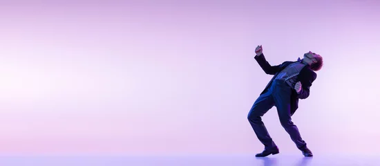 Fototapeten Porträt eines jungen, stilvollen Mannes in Vintage-Retro-Stil-Kleidung, der Swing-Tanz einzeln auf lilafarbenem Hintergrund im Neonlicht tanzt © master1305