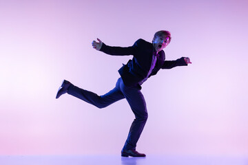 Portrait of young stylish man in vintage retro style clothes dancing swing dance isolated on lilac color background in neon light