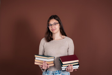 A beautiful and smart girl student is holding books in her hands, preparing for the exam. A woman stands on a brown background.