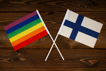 Rainbow flag LGBT and flag of Finland on beautiful brown background with wooden texture. LGBT Pride...