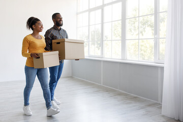 Fototapeta na wymiar Cheerful glad millennial african american husband and wife carry cardboard boxes and moving