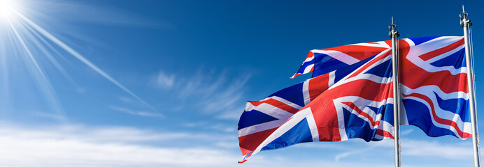 Two national UK flags with flagpole, blowing in the wind on a blue sky with clouds and copy space...