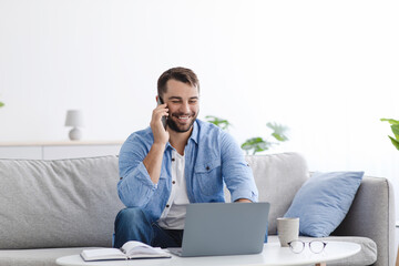 Cheerful mature caucasian male manager have call, working on laptop in living room