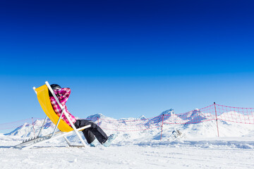 girl sunbathing near a snowy ski slope with blue sky background