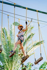a teen girl in a helmet, T-shirt and shorts climbs in a rope park