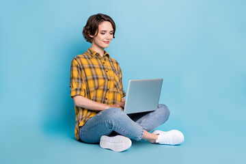 Photo of pretty focused lady sit floor remote work netbook wear checkered shirt isolated blue color background