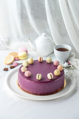 whole cake in violet glaze decorated macaroons and cup of tea on the table