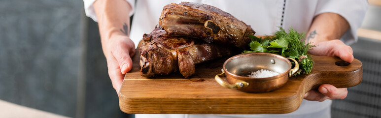 Cropped view of chef holding delicious meat on cutting board, banner
