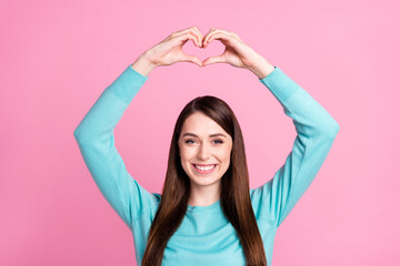 Portrait of attractive cheerful girl showing heart sign over head isolated over pink pastel color background