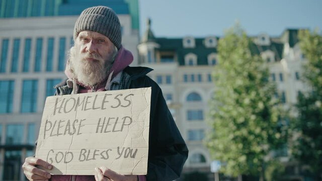 Homeless male holding please help sign, looking at camera, urban charity, need