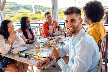 Portrait of young man with group of friends at reunion eating and drinking wine.