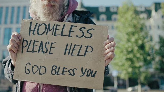 Senior man in need showing homeless cardboard sign asking for help in the street