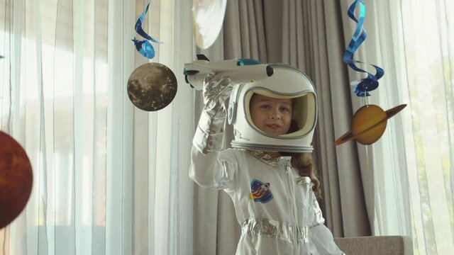 Creative spacewalk dreamer. Fantasy child astronaut flying in spaceship.Spacewoman form of space hero in suit bumblebee astronaut conquers space in her children's room,interior hung with planets.