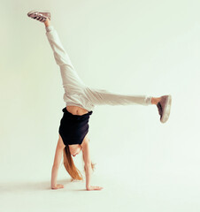 Attractive flexible teenage girl doing handstand on light background