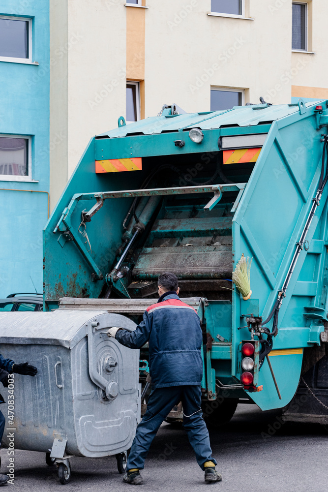 Aufkleber A garbage truck picks up garbage in a residential area. Workers load a container with garbage. Separate collection and disposal of garbage.