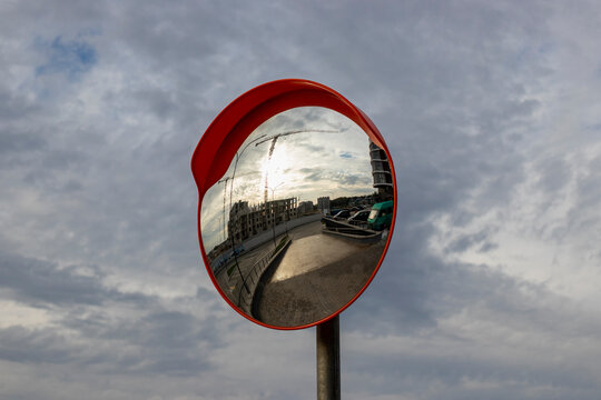 Outdoor panoramic mirror for safe exit from the parking lot with the reflection of a monolithic building under construction.