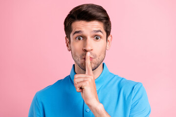 Photo of young serious brown haired male showing silence gesture shut up isolated on pink color...