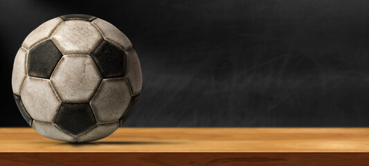 Closeup of an old leather soccer ball on a wooden table with empty blackboard on the background...