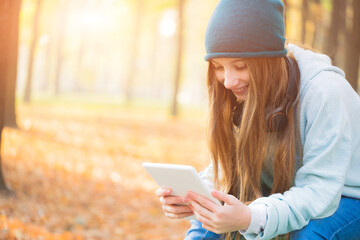 Obraz premium Smiling girl reading on tablet sitting in park