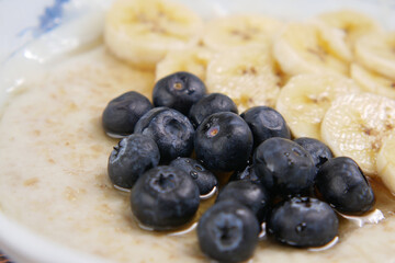 a bowl of oats, berry, banana and honey on table 