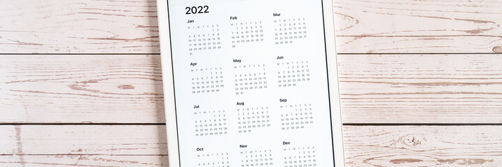 tablet computer with an open app of calendar for 2022 year on a wooden boards background. concept business or to do list goals with technology using. top view, flat lay. banner