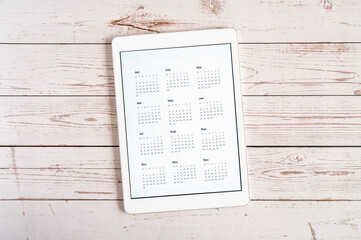 tablet with an open app of calendar for unspecified unknown date year without date on a wooden boards background. concept business or to do list goals with technology using. top view, flat lay