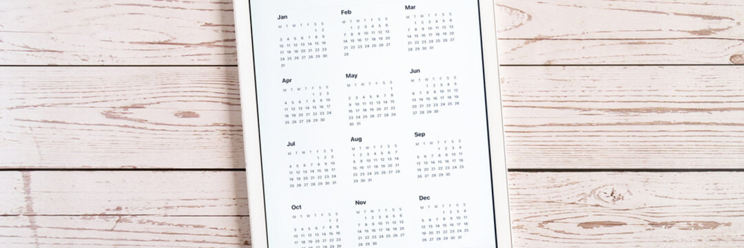 tablet computer with an open app of calendar for unspecified unknown date year without date on wooden boards background. business or to do list goals with technology using. top view, flat lay. banner