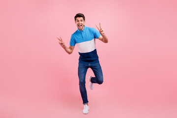 Full size photo of cool brunet young guy go show v-sign wear polo jeans sneakers isolated on pink background