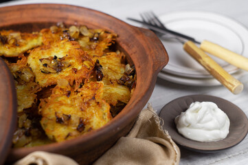 Potato pancakes with fried onions and sour cream in a ceramic pan