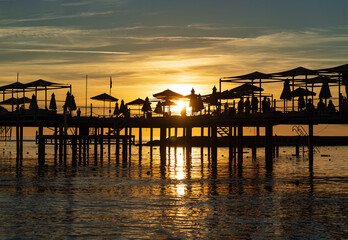 Fototapeta na wymiar pier with umbrellas and sunbeds. silhouettes. beautiful sunset on sea. 