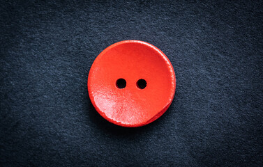 Close up view of red wooden sewing button on dark cloth