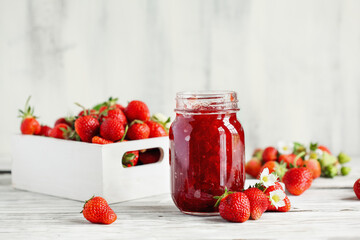 Homemade strawberry preserves or jam in a mason jar surrounded by fresh organic strawberries....