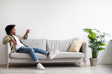 Black Man Turning On Air Conditioner With Remote Controller At Home