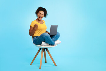 Fototapeta na wymiar Cool young black woman sitting on chair with laptop, gesturing YES, winning casino bet or online game, shopping on web