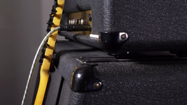 Closeup POV dolly shot of an electric guitar leaning against a vintage valve amplifier and speaker cabinet, with an instrument lead / cable / cord plugged in.