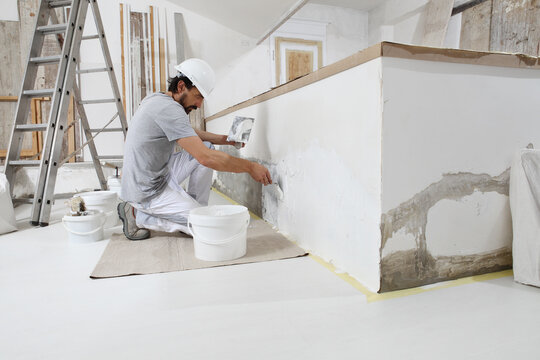 plasterer man at work, take the mortar from the bucket with trowel to plastering the wall of interior construction house site and wear helmet,
